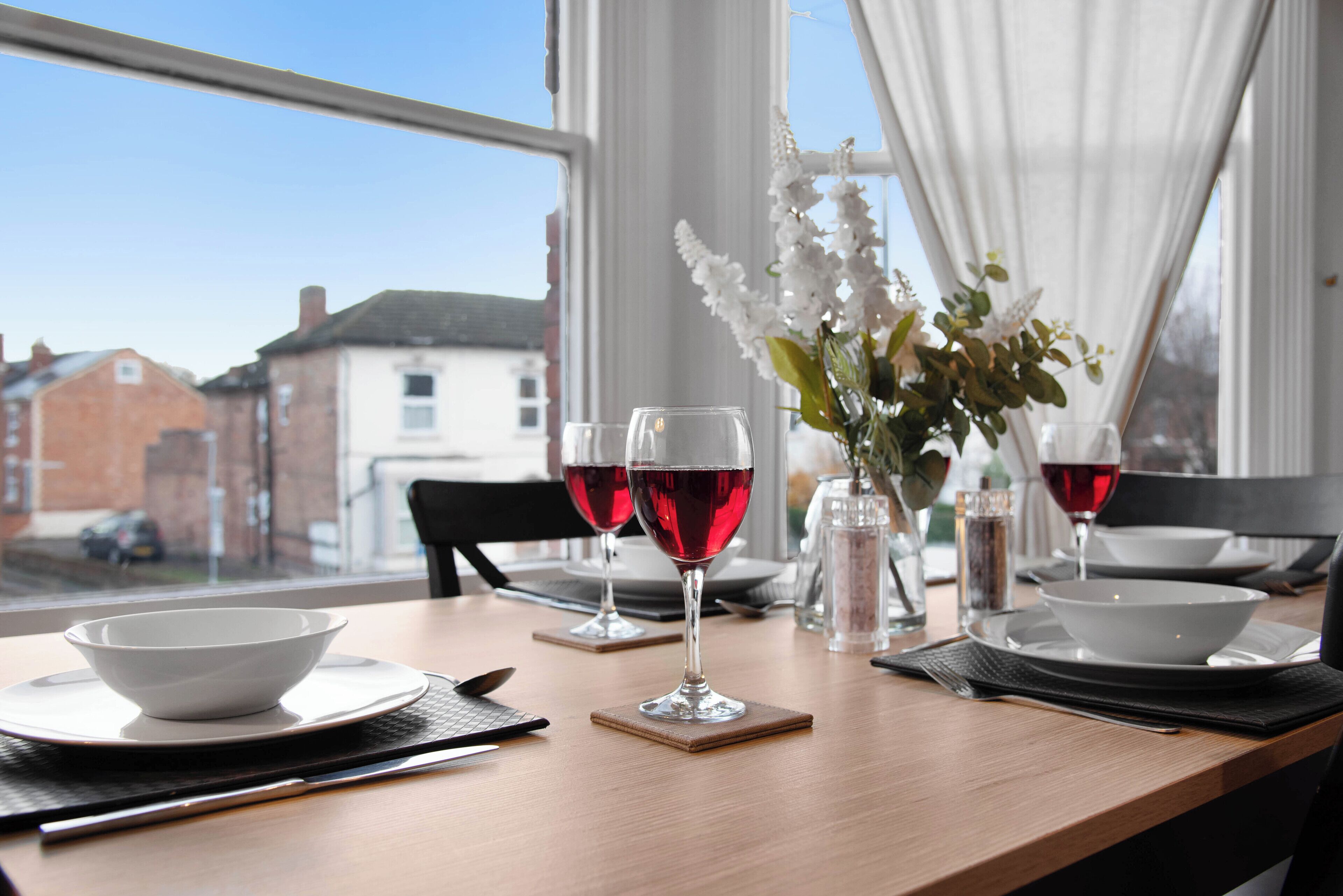 A dining table with two wine glasses, a bowl, and a vase with flowers.