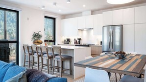 Een moderne keuken met witte kastjes, een roestvrijstalen koelkast en een eethoek met een houten tafel en stoelen.