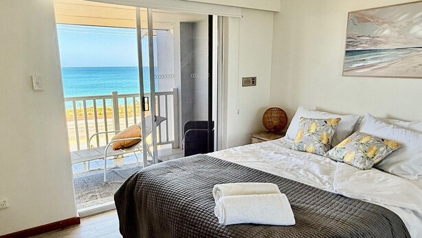 A bedroom with a bed, a view of the beach, and a door leading to a balcony.