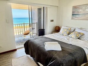 Une chambre avec un lit, une vue sur la plage et une porte donnant sur un balcon.