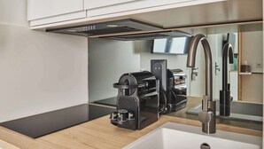 Cocina moderna con una elegante máquina de café negra, un lavamanos de acero inoxidable y un espejo grande que refleja la habitación.