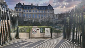 Una entrada con portón a un edificio histórico, con un cartel que prohíbe perros y un cartel que dice 'Stop Racism'.