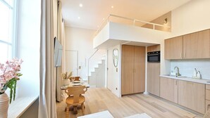 Una cocina moderna con armarios de madera, un comedor con mesa y sillas de madera, y una escalera que sube a un nivel superior.