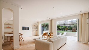 Een ruime woonkamer met een grote bank, een eethoek met houten stoelen en uitzicht op een tuin door grote ramen.