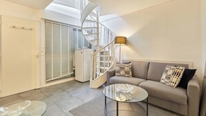 Un salon moderne avec un escalier en colimaçon, un canapé agrémenté de coussins à motifs, une table basse en verre et une lucarne au plafond.