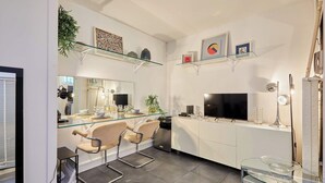 Une cuisine moderne avec une table à manger en verre, des tabourets de bar, un four encastré et un téléviseur.