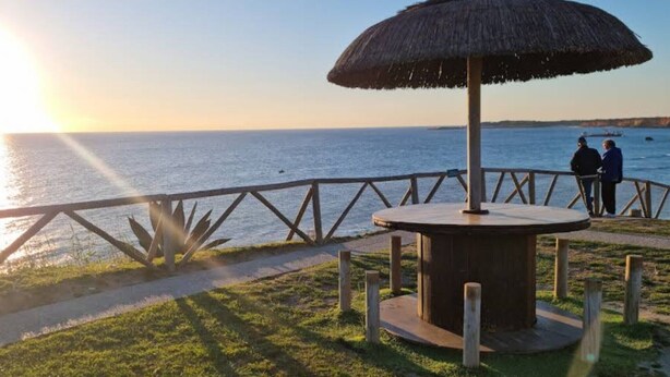 A wooden gazebo with a thatched roof overlooking a body of water, a wooden fence, and a couple of people standing by the railing. - Comfortable Conil Apartment by the Beach (Conil de la Frontera)