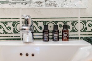 Een wastafel met daarboven drie flessen douchegel, shampoo en bodylotion.