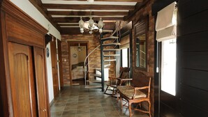 Un couloir avec une porte en bois, un escalier en colimaçon et une fenêtre munie d’un store.