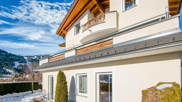 Ein zweistöckiges Gebäude mit Balkon, großen Fenstern und Blick auf eine verschneite Landschaft.