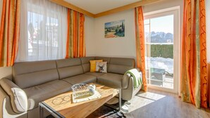 Ein modernes Wohnzimmer mit einem Ecksofa, einem Glastisch und Blick auf eine verschneite Landschaft durch ein großes Fenster.