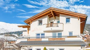 Ein mehrgeschossiges Gebäude mit Balkon, mit der Aufschrift "Apartment Diana", vor einer verschneiten Berglandschaft.