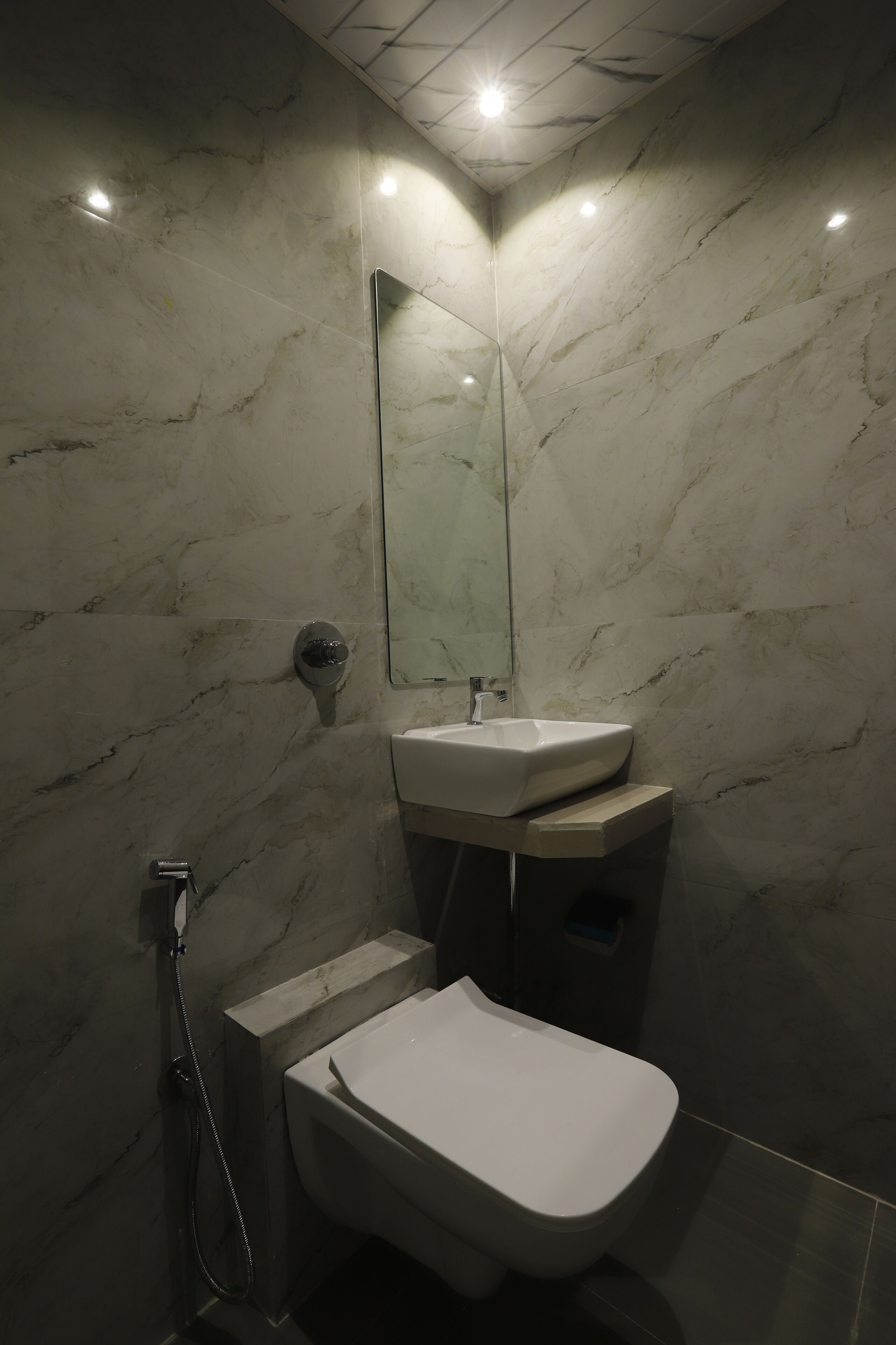 Et moderne badeværelse med en marmorvæg, et håndvask, et toilet og en bruseniche.