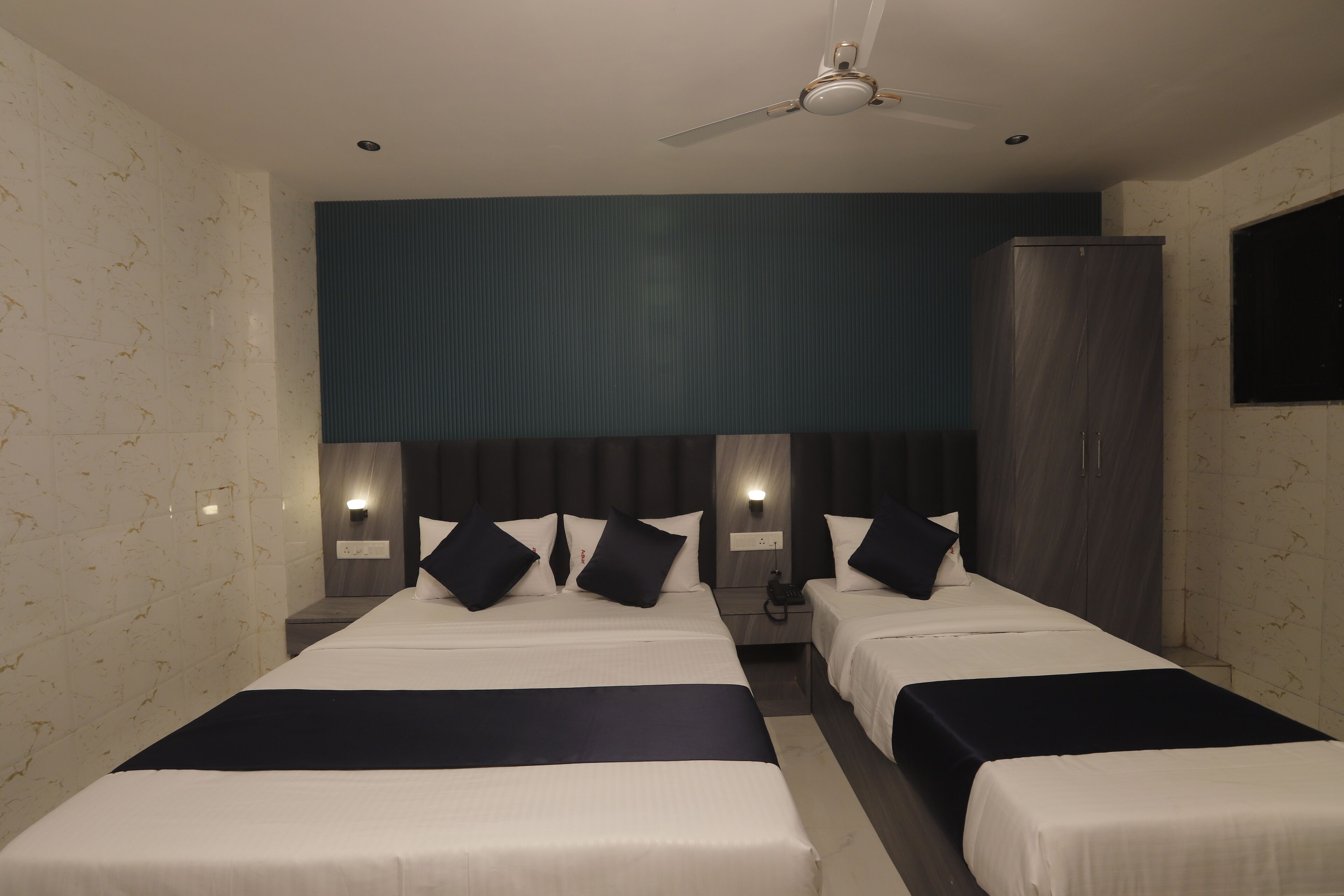 A hotel room with two beds, a ceiling fan, and wall-mounted lights.