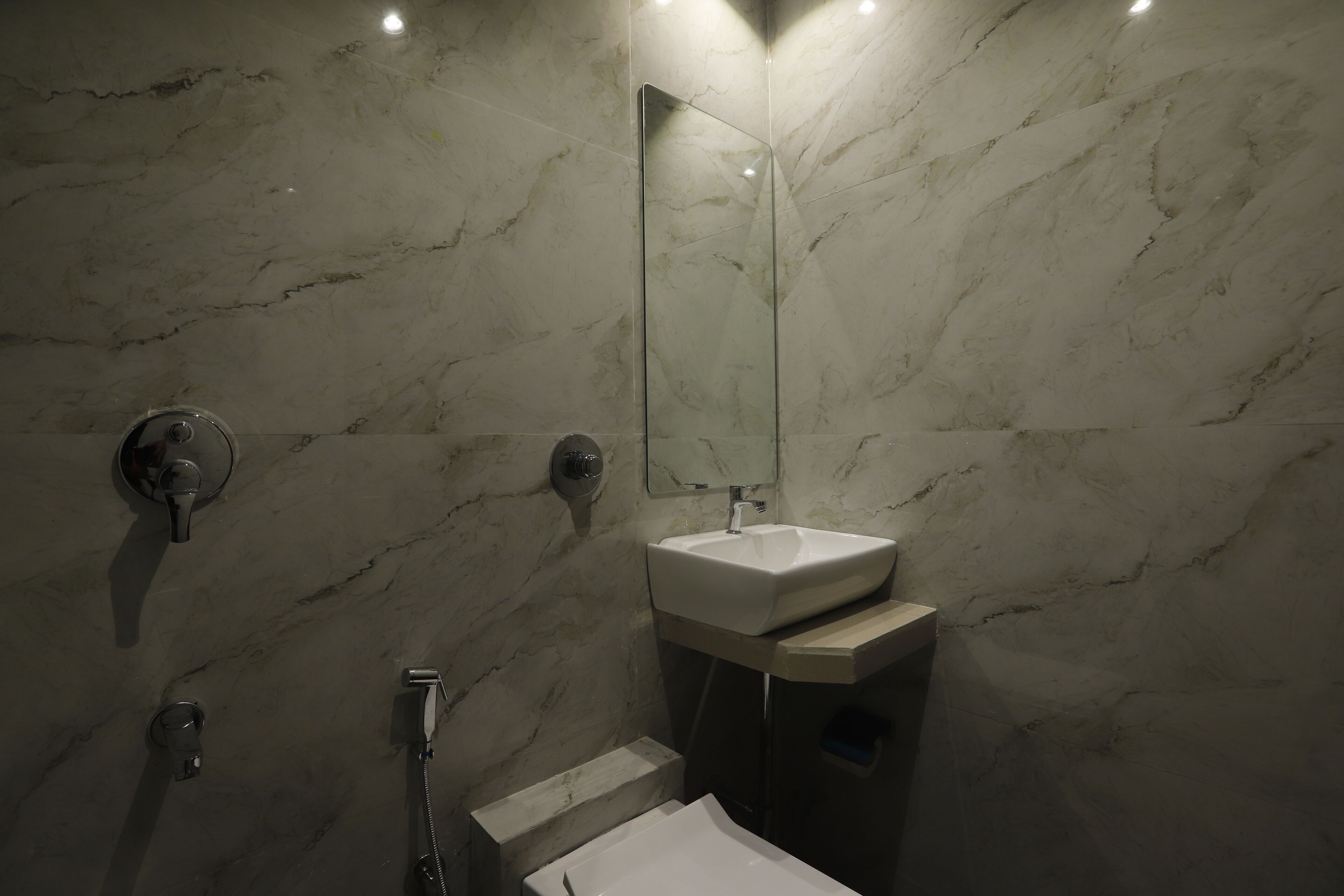 A bathroom with a marble wall, a sink, a mirror, and a shower.