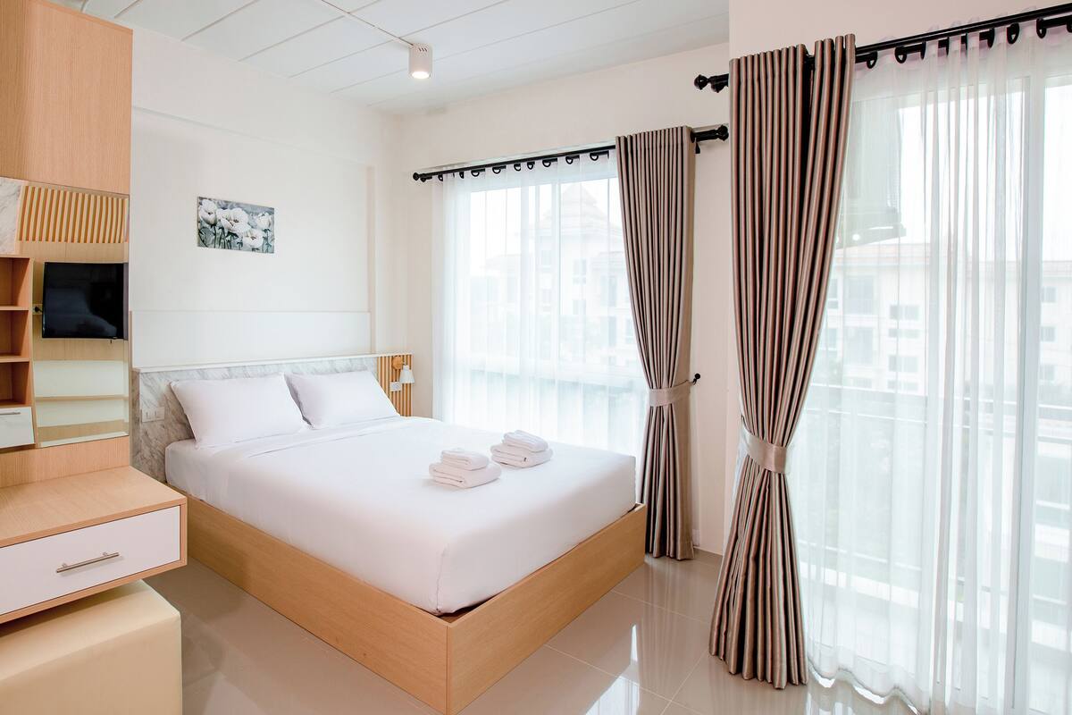 Una habitación de hotel moderna con una cama de madera, un armario empotrado y un ventanal con cortinas.