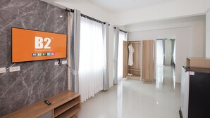 Una habitación de hotel moderna con una pared de mármol, un televisor mostrando 'B2 Boutique&Budget', un banco de madera, un vestidor y un refrigerador negro.