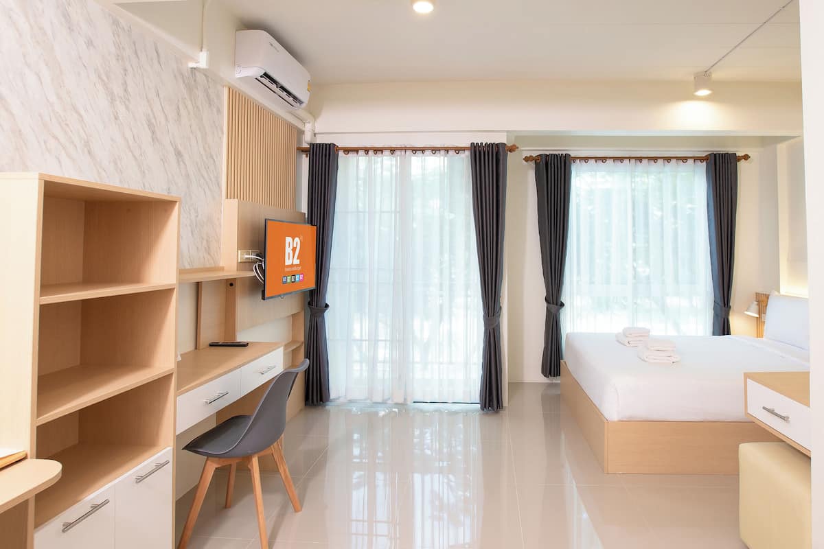 Una habitación de hotel con una cama, un escritorio con una silla, un televisor y un armario.