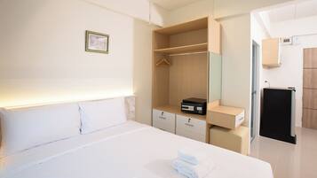 A hotel room with a bed, a bedside table, a wardrobe, a mirror, and a small desk with a computer.