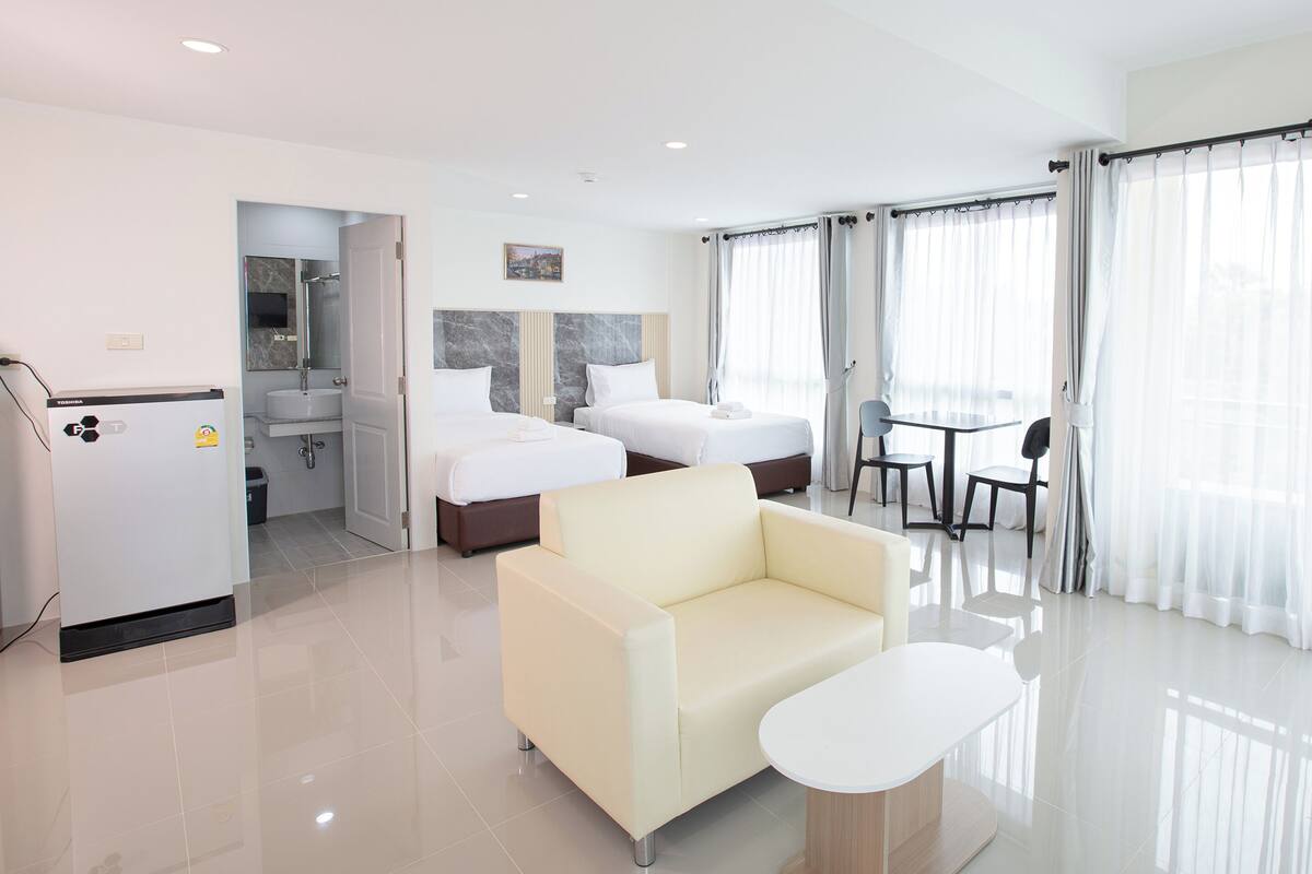 Una habitación de hotel moderna con sofá, una mesita, cama, baño y balcón con cortinas.