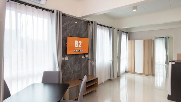 A modern hotel room with a large flat-screen TV mounted on a marble wall, a wooden desk, and a seating area with a chair.