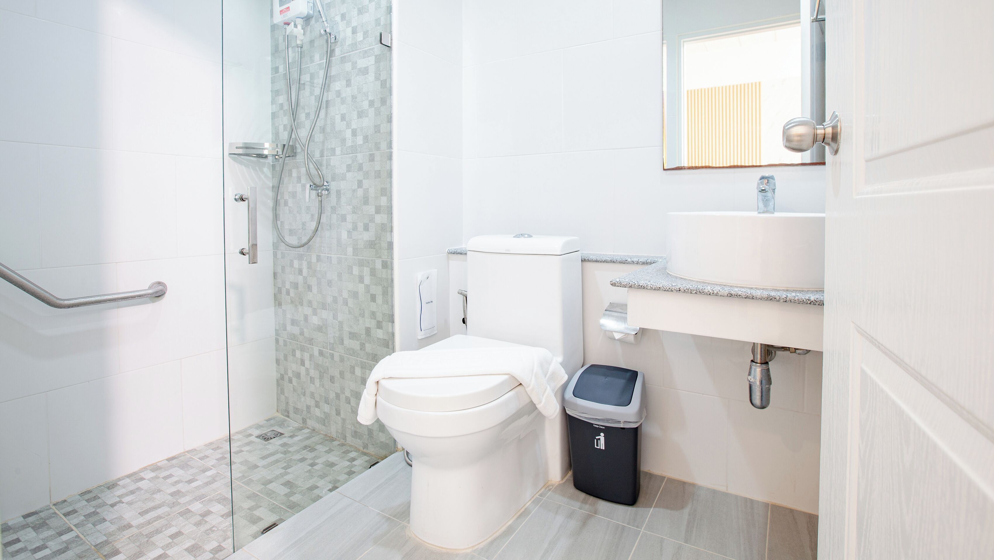 A modern bathroom with a glass shower enclosure, a white toilet, a sink with a mirror, and a trash bin.