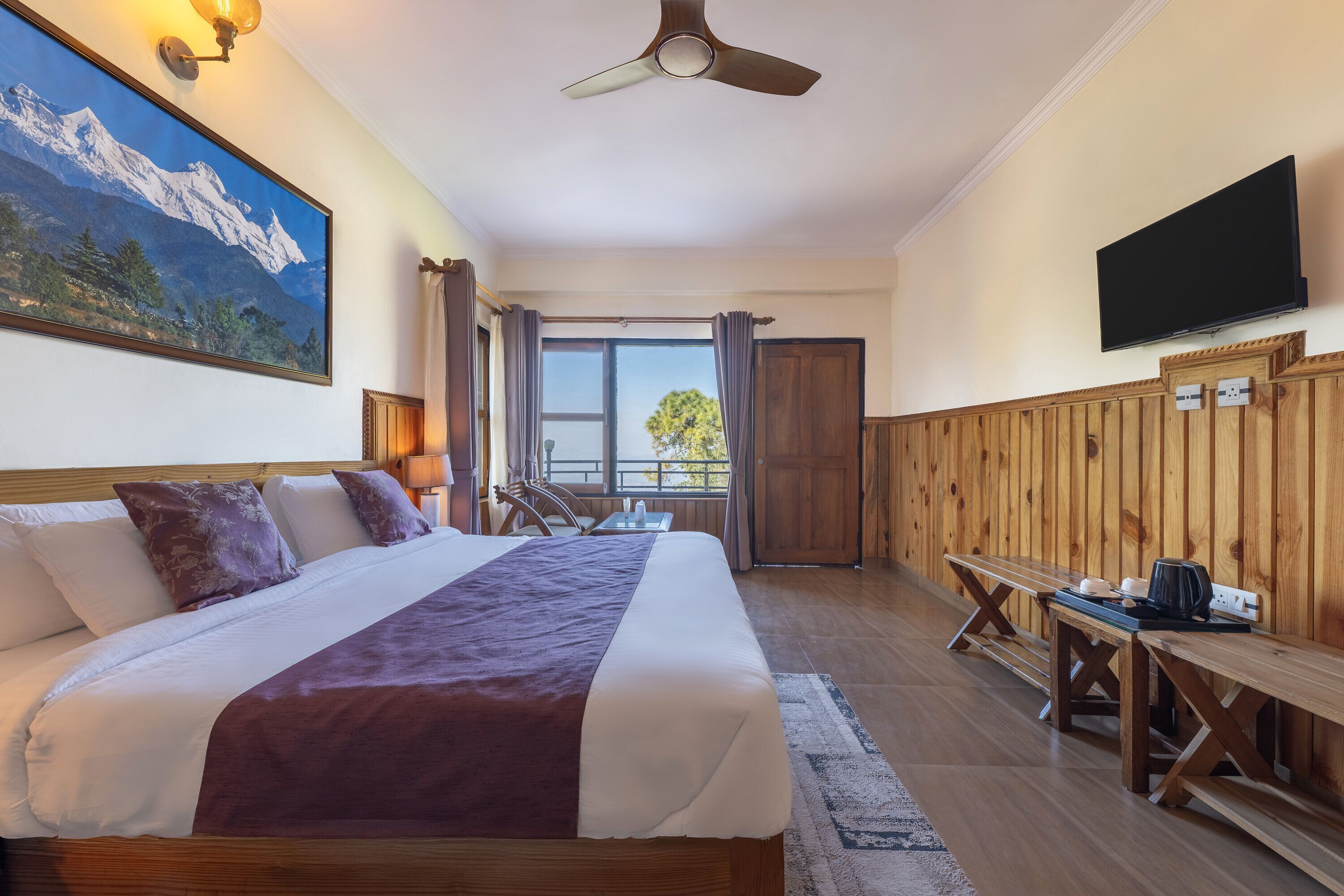 A hotel room with a bed, a desk, a TV, and a painting of a mountain.