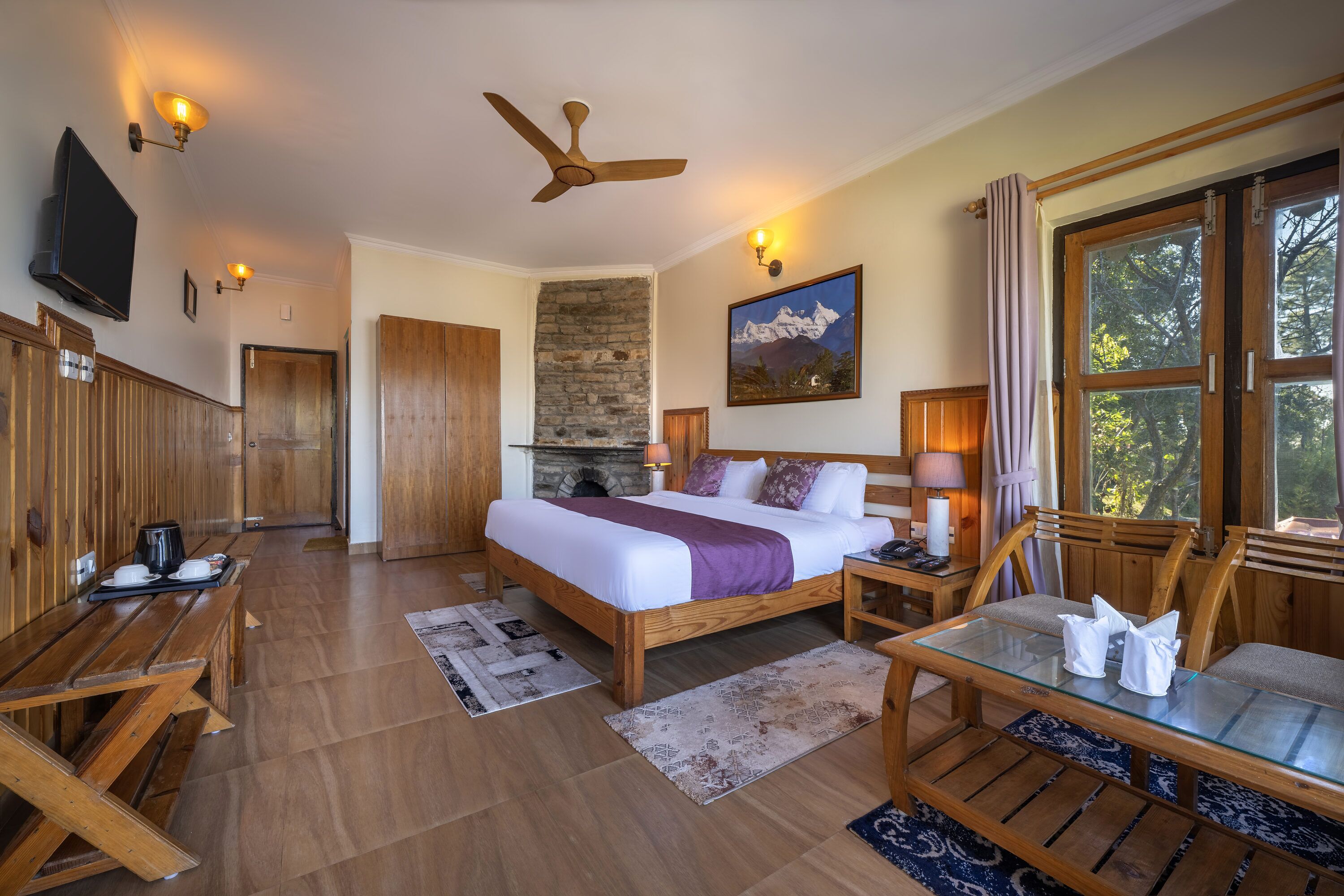 Un dormitorio amplio con una cama grande, muebles de madera, una chimenea de piedra y vistas a árboles por la ventana.