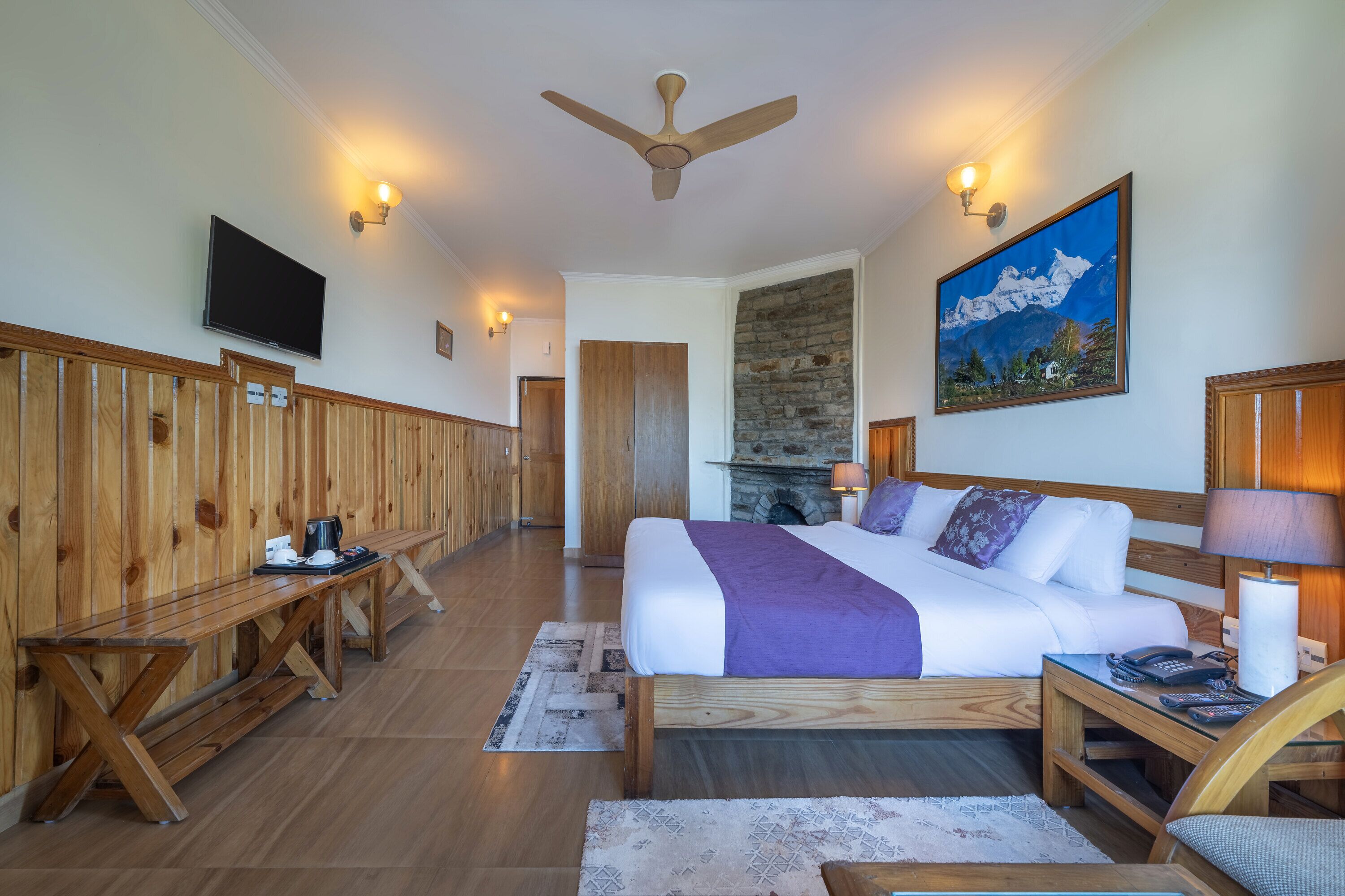 Quarto de hotel com uma cama grande, móveis de madeira, lareira de pedra e televisão na parede.
