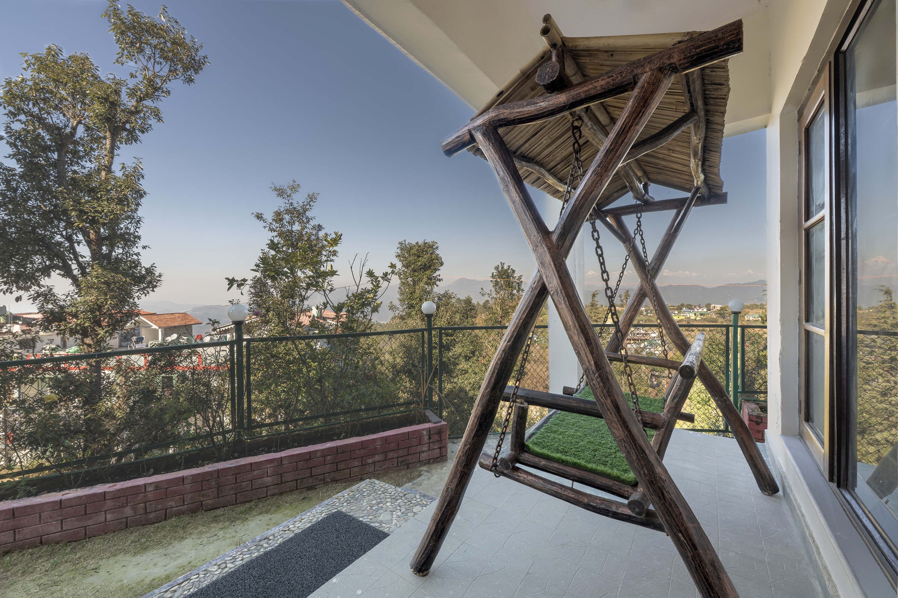 Un balcón con una hamaca de madera, vista a la ciudad y un muro de ladrillo.