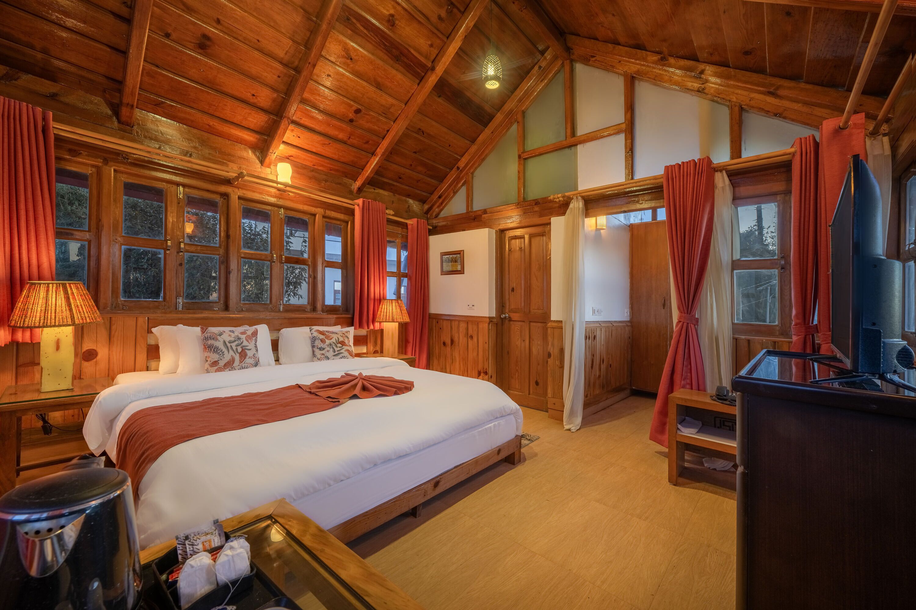 A wooden cabin-style bedroom with a large bed, wooden walls, and a ceiling with exposed beams.