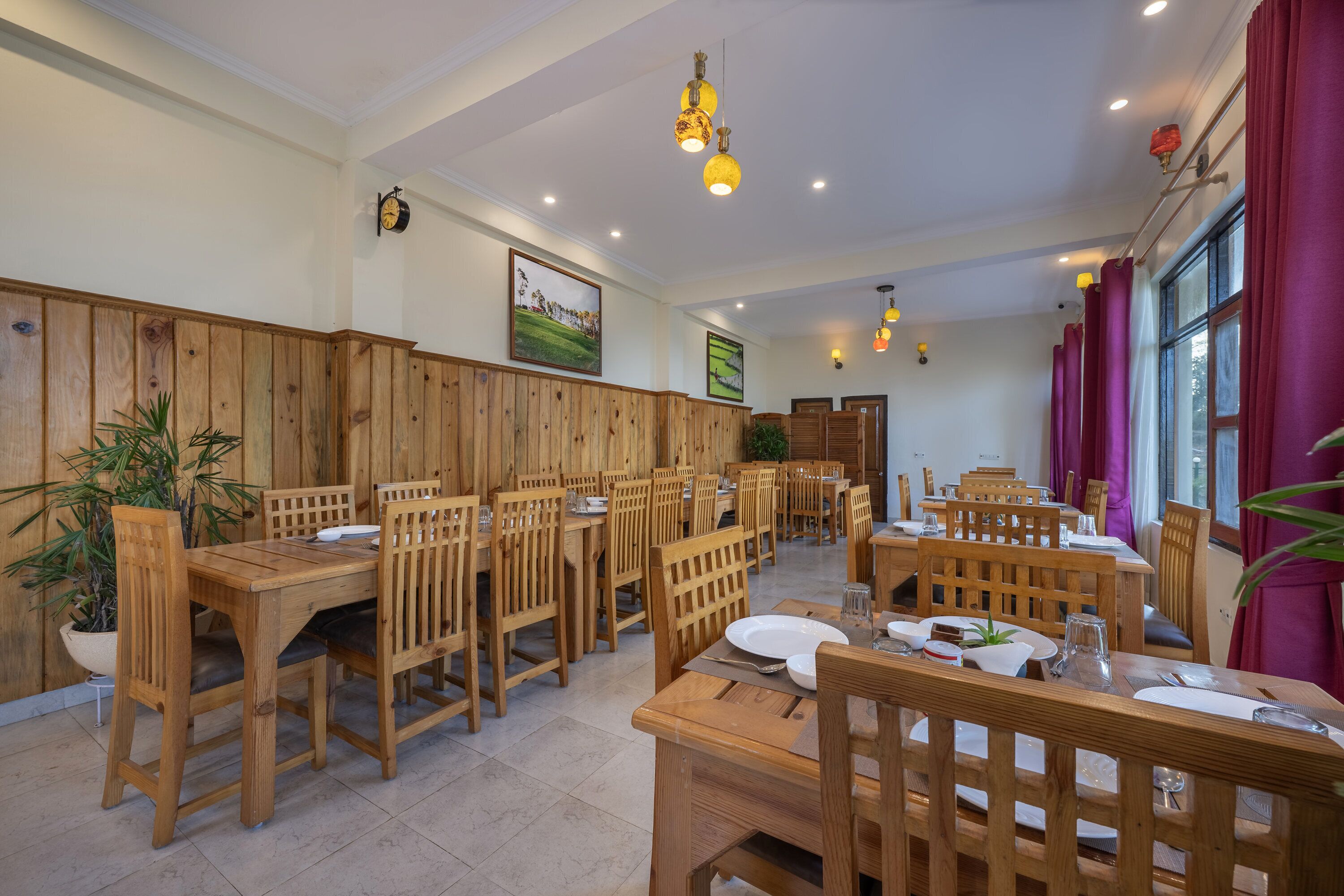 Un restaurant avec des tables et des chaises en bois, des plantes en pot et des œuvres d’art encadrées accrochées aux murs.
