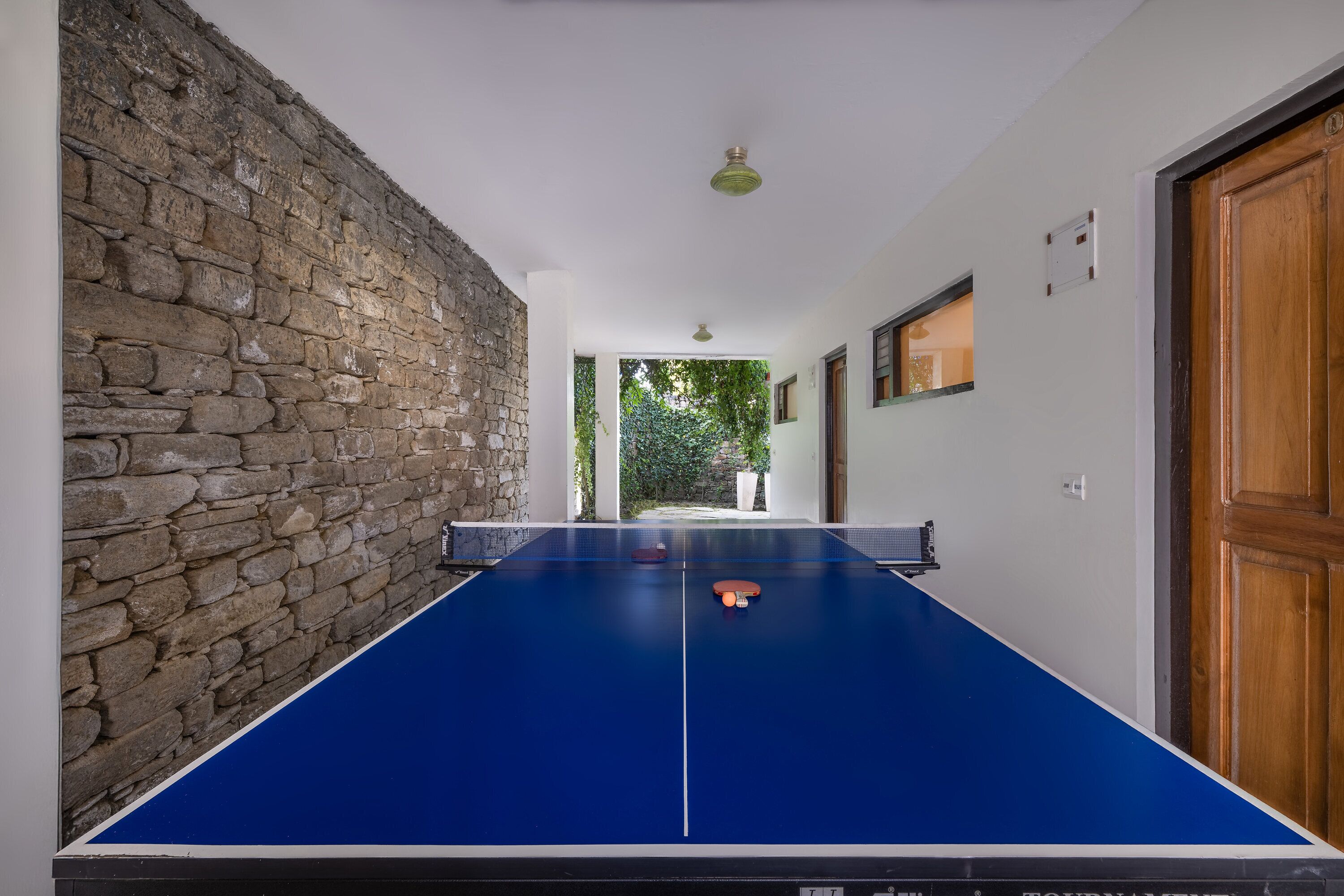 Una mesa de ping pong en un pasillo con paredes de piedra y una puerta de madera.