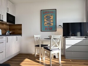 Una cocina moderna con armarios blancos, un microondas, una mesa de comedor con sillas y un cartel enmarcado en la pared.
