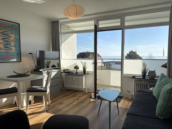 Sala moderna com vista para o mar, área de jantar e televisão.