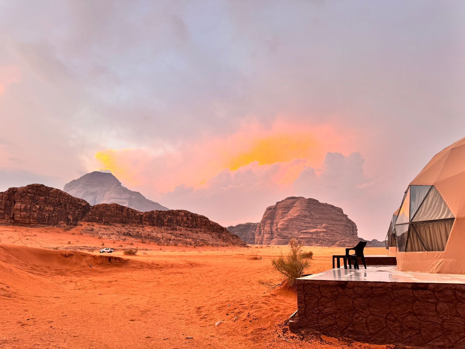 A desert landscape with a tented accommodation featuring a stone wall and a table with chairs.