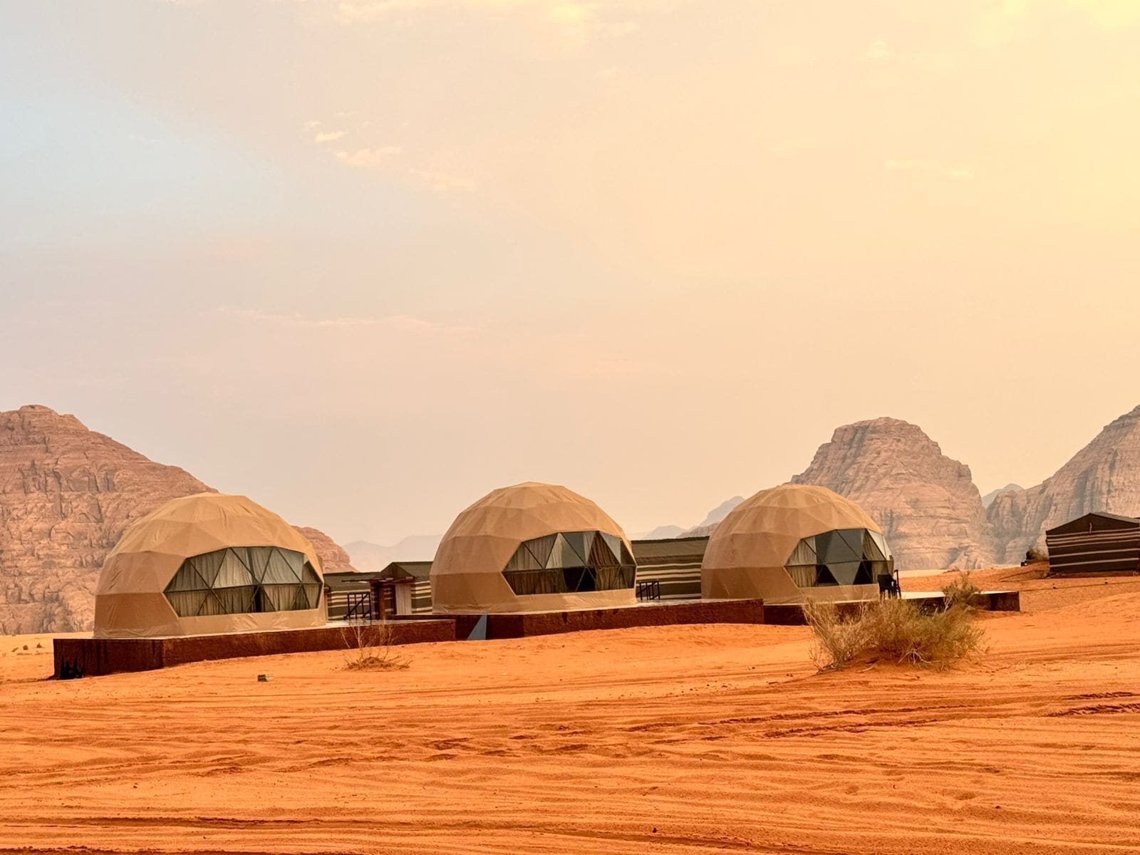 A row of dome-shaped tents in a desert landscape with rocky mountains in the background.
