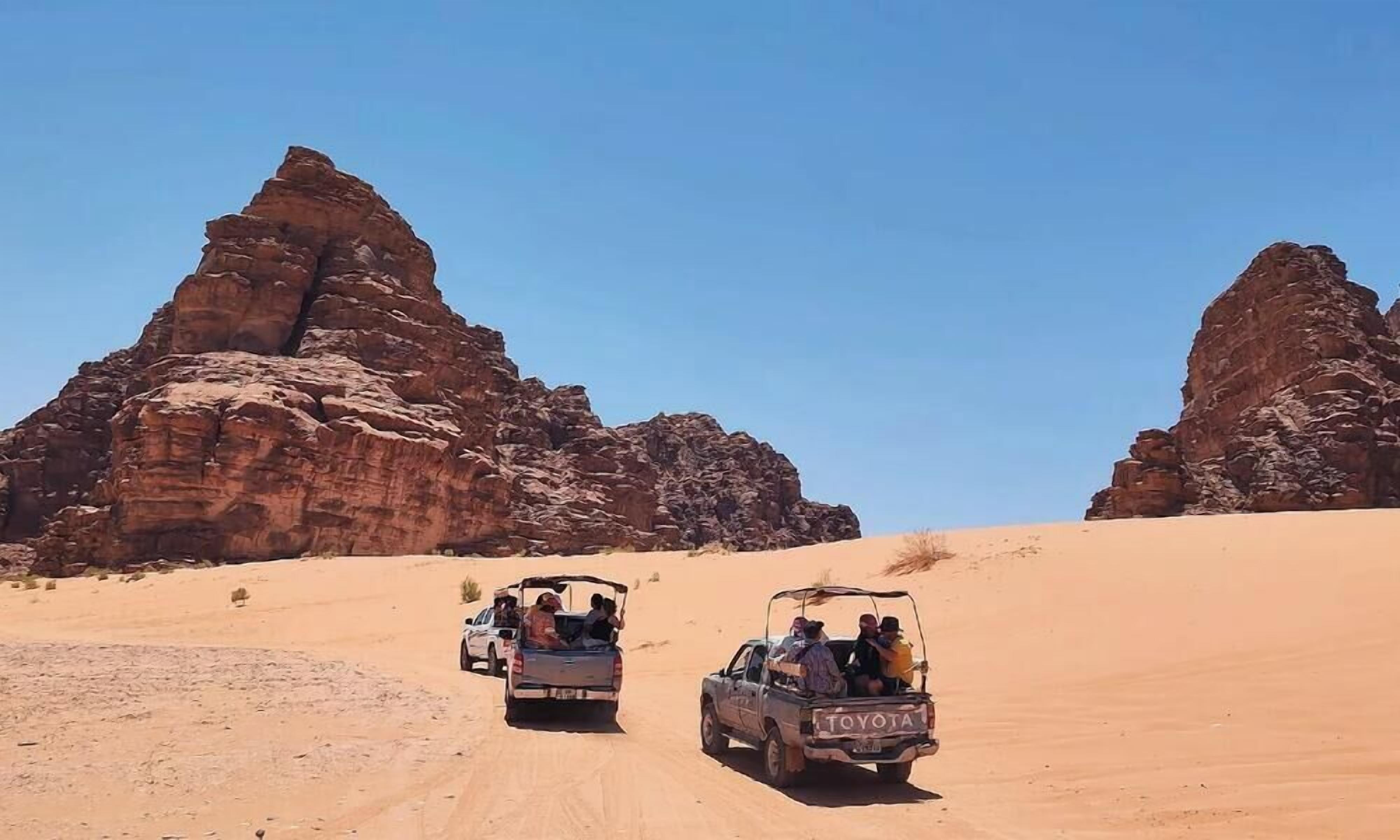 Two off-road vehicles on a sandy path with rocky formations in the background.