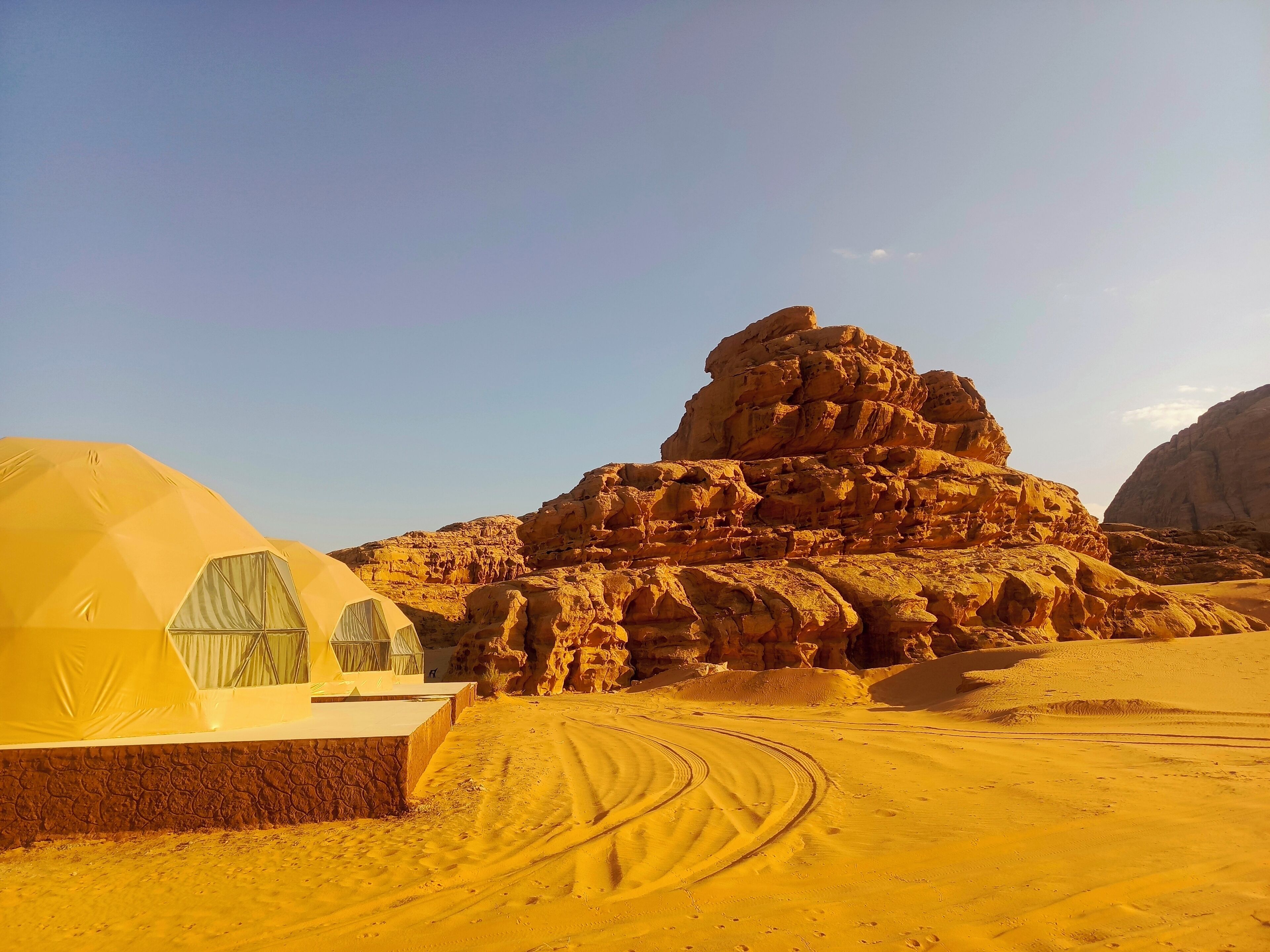 A desert landscape with a prominent rock formation and a tented area with a view of the scenery.