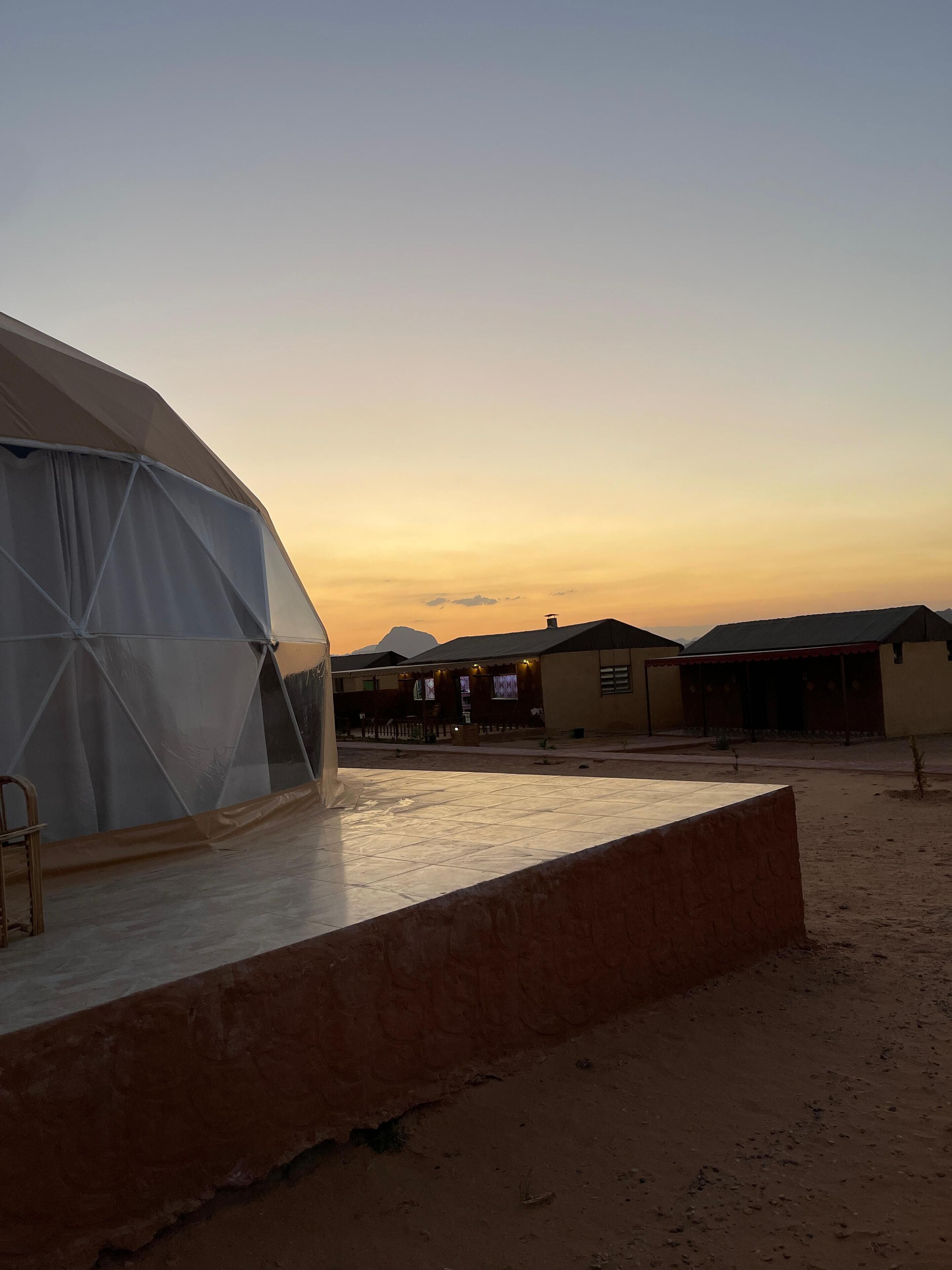 A desert landscape with a large tent-like structure, a few buildings, and a clear sky.