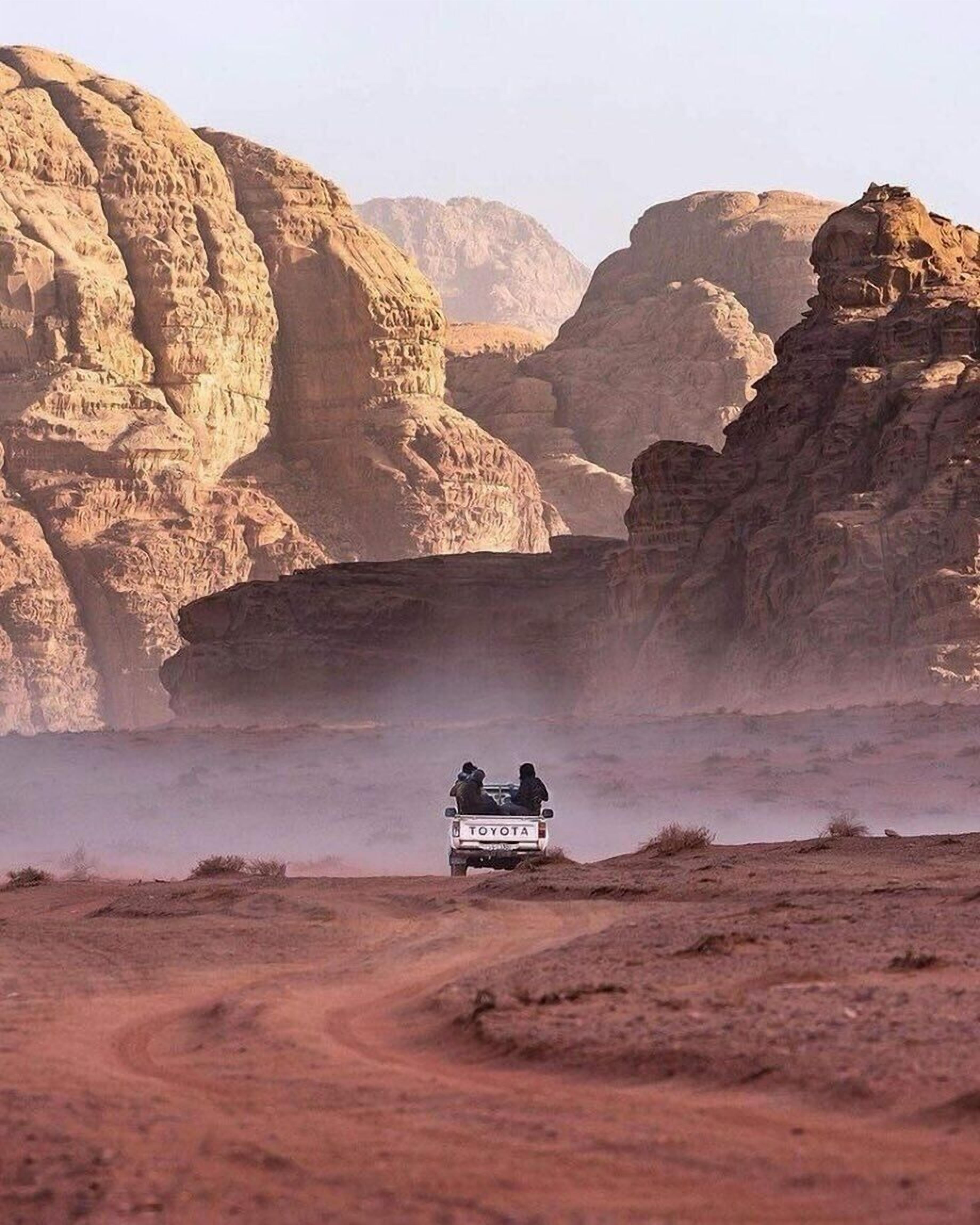 A Toyota vehicle driving on a dusty road with rocky cliffs in the background.