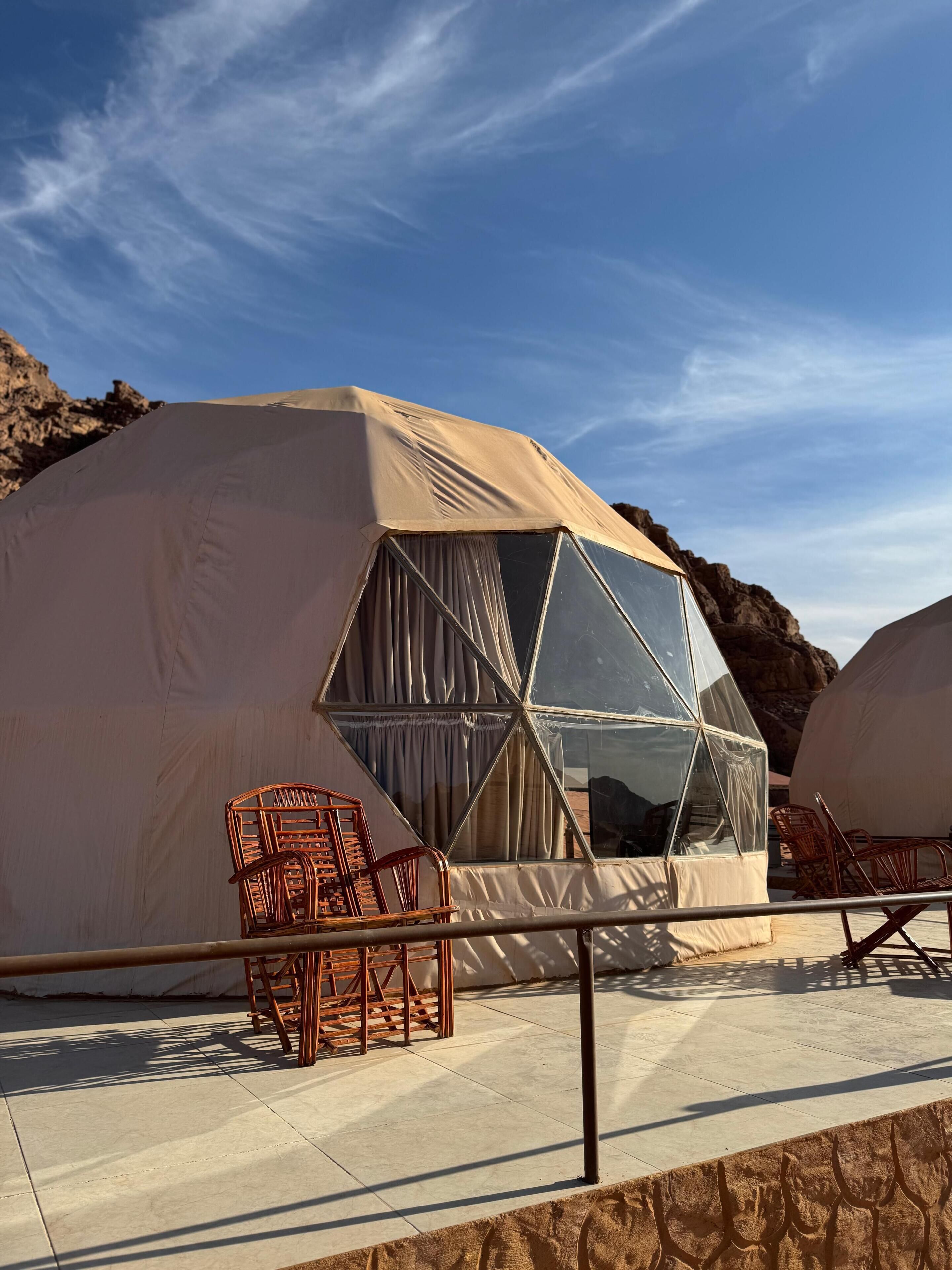 A geodesic dome structure with a reflective interior, surrounded by outdoor seating and a clear sky.