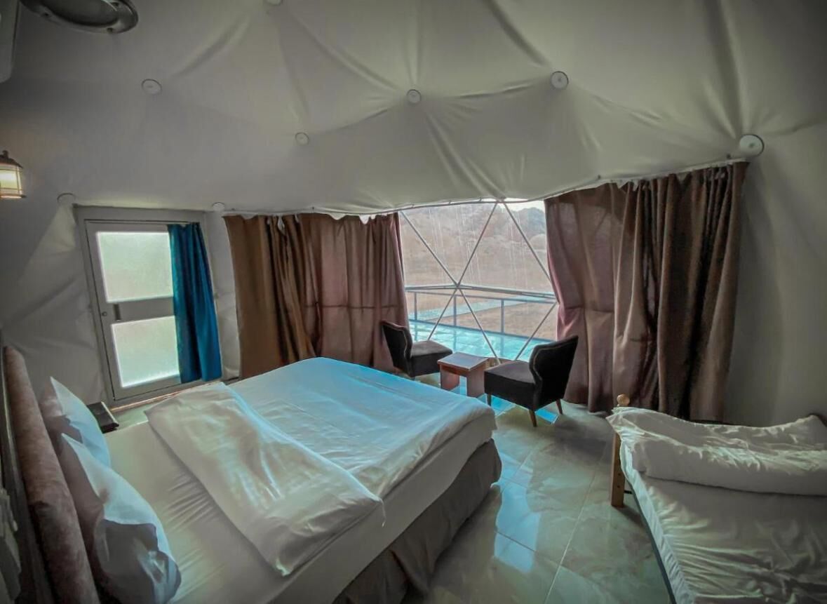 A room with a bed, a small table, two chairs, and a view of a pool.
