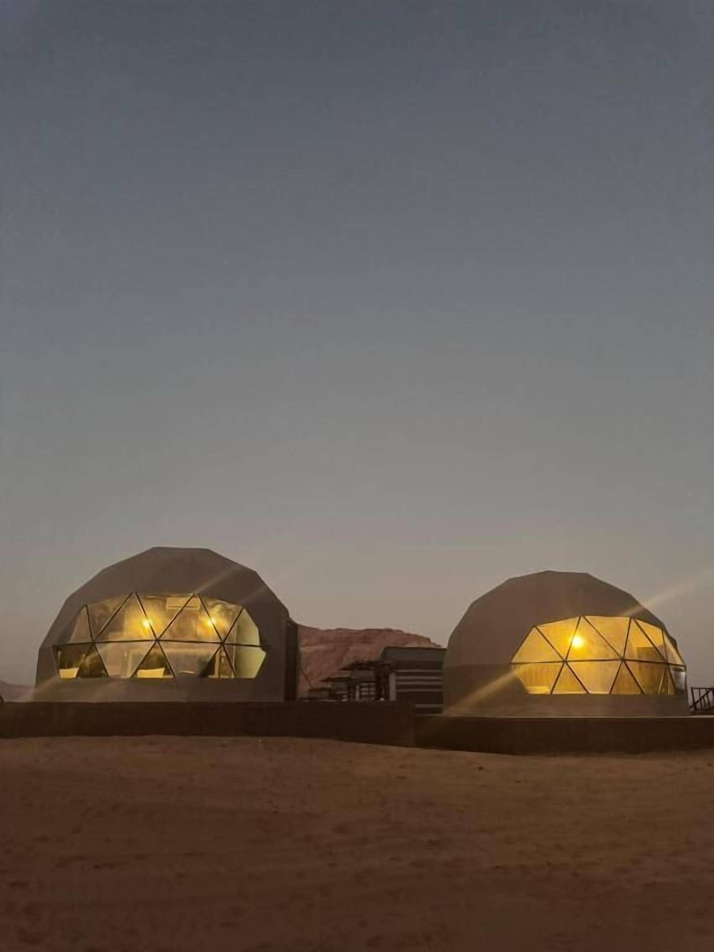 Due strutture a forma di cupola illuminate dall'interno, sullo sfondo di un paesaggio desertico.
