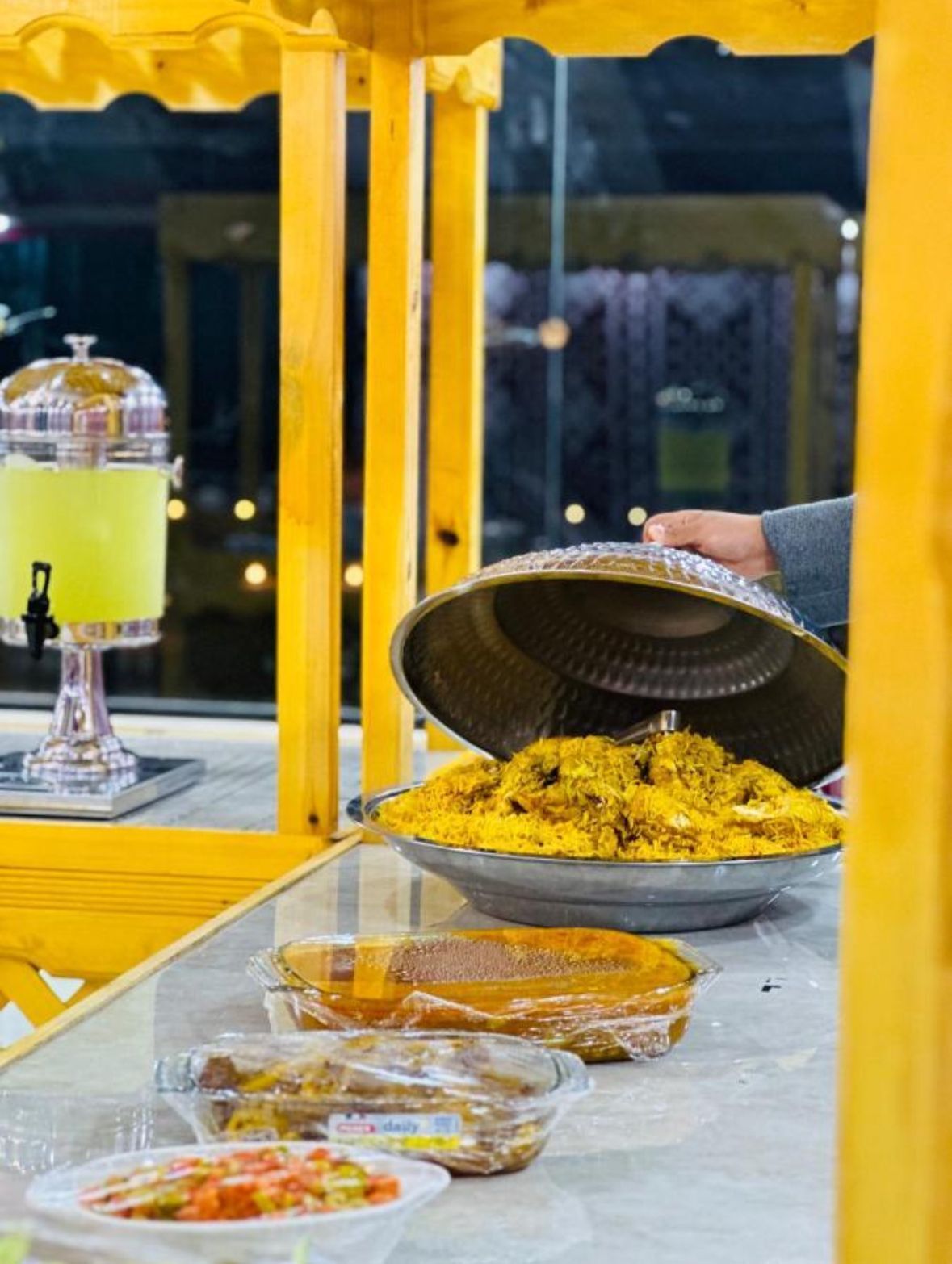 Un buffet proposant une variété de plats, notamment un grand saladier de riz jaune, une carafe de boisson jaune et plusieurs autres plats présentés dans des récipients en verre.