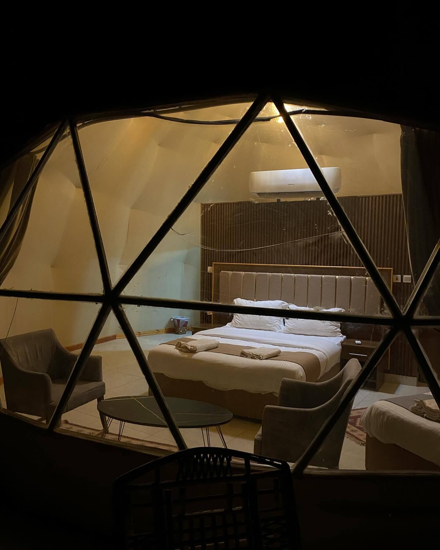 Una habitación en forma de cúpula geométrica con una cama, dos sillas y una pequeña mesa.