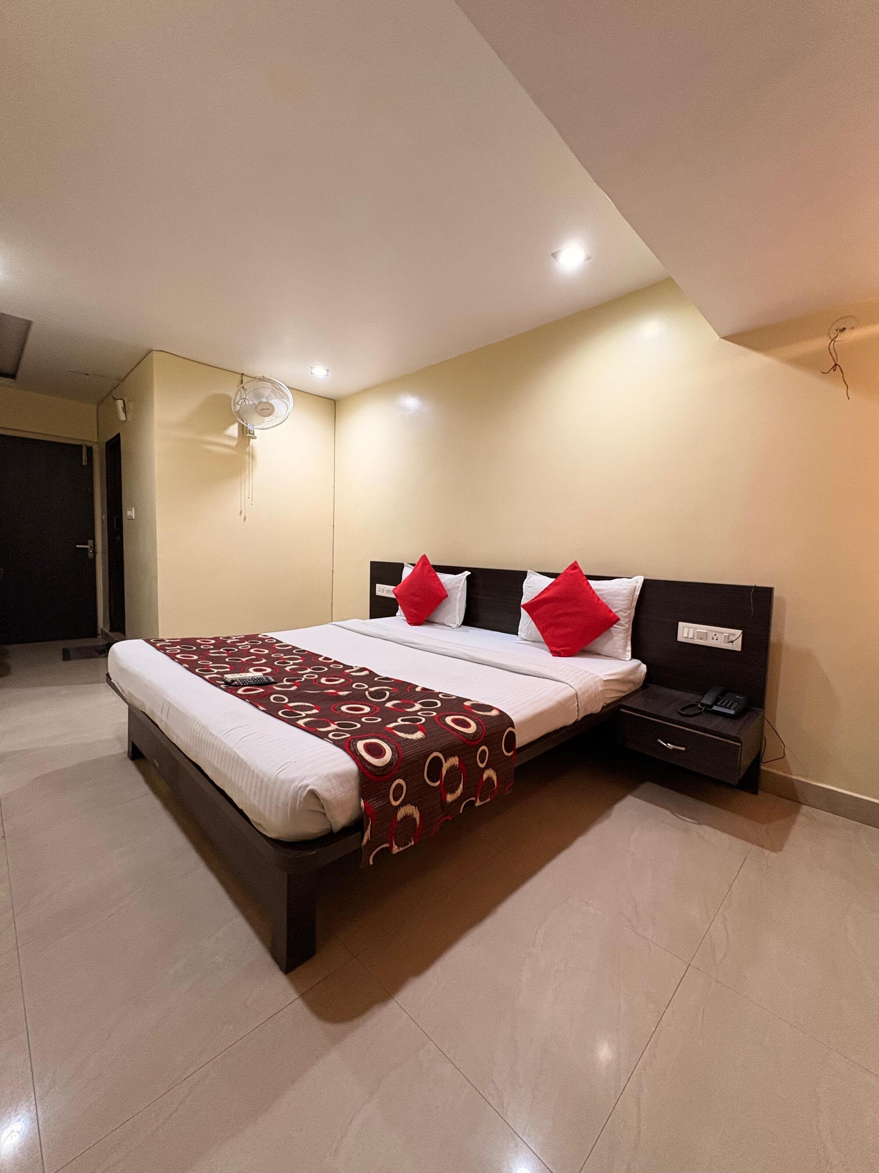 Habitación de hotel ordenada con cama, mesita de noche y ventilador de pared.
