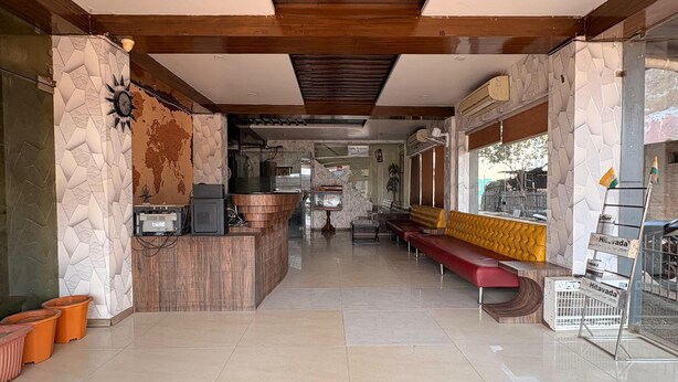 A spacious lobby with a central reception desk, a red bench, and a view of the kitchen area. - Hotel Welfare Club (Bhilai)