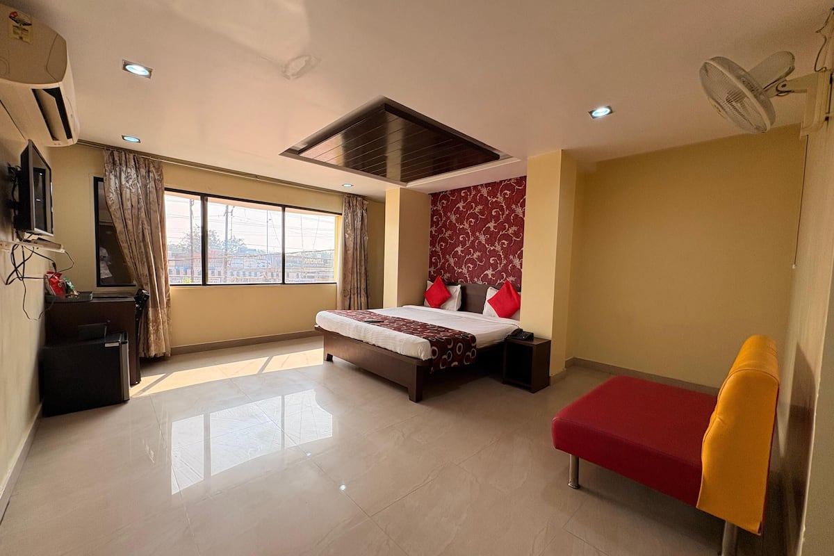 A hotel room with a bed, a desk, a chair, a window, and a ceiling fan.