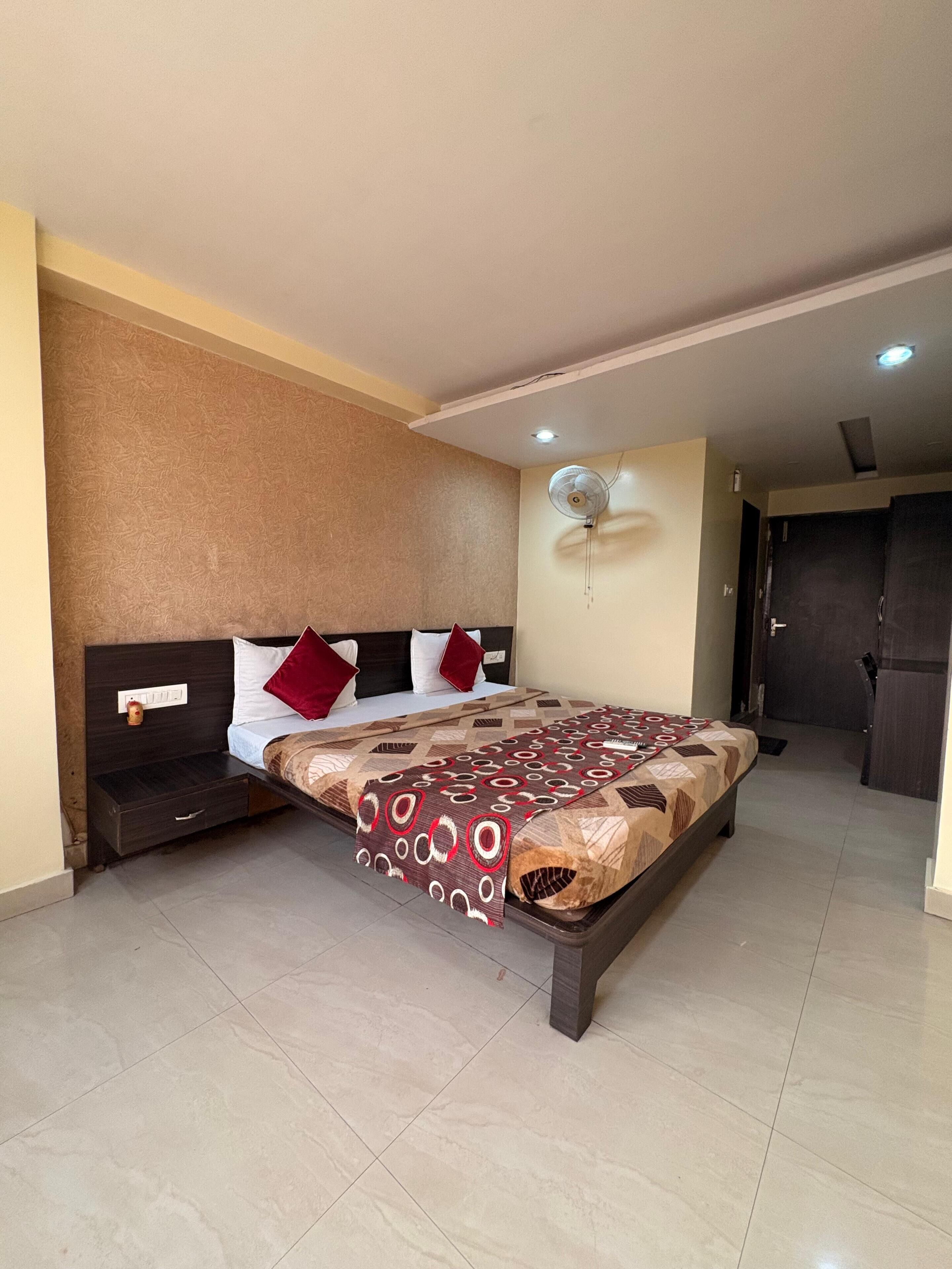 A hotel room with a bed, a bedside table, a wall-mounted fan, and a door.